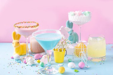 Colorful pastel colored kids Easter party mocktails, Creamy and iced non-alcohol drinks with cotton candy, marshmallow, sugar sprinkles and Easter eggs, on blue pink pastel background copy space