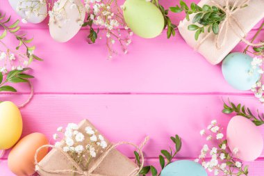 Pink Easter greeting card background with spring flowers, green leaf branches and colorful pastel Easter eggs, top view copy space