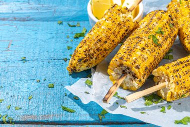 Sweet corn grilled with butter, cheese, cilantro and herbs. Vegetarian, healthy, clean eating barbeque food. Portioned bbq grill corn cobs on high-colored blue wooden background