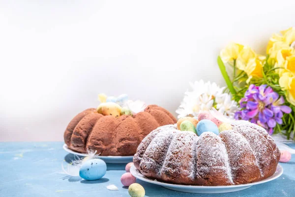Traditional cake for Easter. Chocolate and vanilla Easter round cake with chocolate and sugar powder sprinkles, colorful Easter eggs, spring flowers, on a blue background copy space