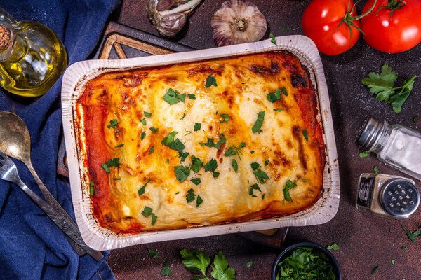 Homemade cannelloni pasta, big tray with baked cannelloni with minced meat with bechamel sauce,with herbs in ingredient on dark background