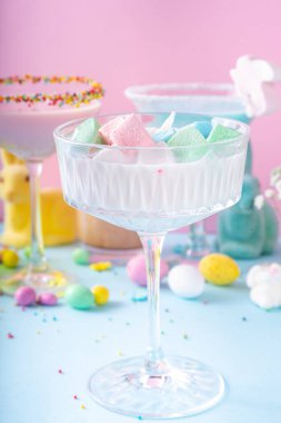 Colorful pastel colored kids Easter party mocktails, Creamy and iced non-alcohol drinks with cotton candy, marshmallow, sugar sprinkles and Easter eggs, on blue pink pastel background copy space