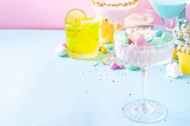 Colorful pastel colored kids Easter party mocktails, Creamy and iced non-alcohol drinks with cotton candy, marshmallow, sugar sprinkles and Easter eggs, on blue pink pastel background copy space