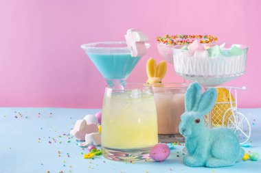 Colorful pastel colored kids Easter party mocktails, Creamy and iced non-alcohol drinks with cotton candy, marshmallow, sugar sprinkles and Easter eggs, on blue pink pastel background copy space