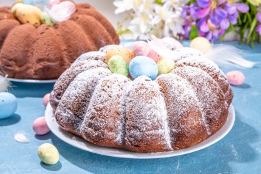 Traditional cake for Easter. Chocolate and vanilla Easter round cake with chocolate and sugar powder sprinkles, colorful Easter eggs, spring flowers, on a blue background copy space