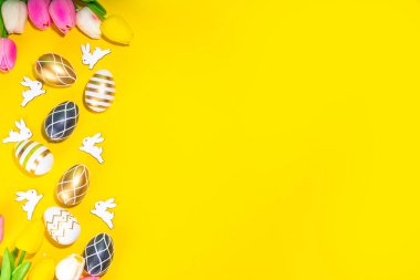 Parlak Paskalya tebrik kartı geçmişi. Renkli siyah, altın renkli, çizgili, beyaz tavşan desenli Paskalya yumurtaları, yüksek renkli sarı arka planda lale çiçeği, düz kopya alanı