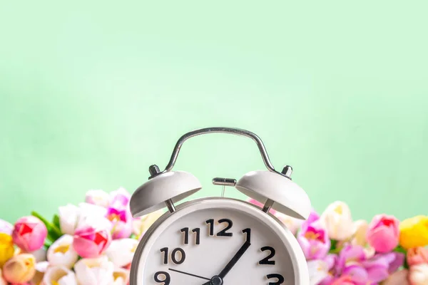 Spring Time Change flatlay. Summer back concept. White Retro Vintage alarm Clock with fresh, beautiful white spring flower on pastel green background, wide bouquet banner background copy space