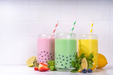Üç renkli yaz köpüklü çay seti, parlak kremalı inci çayı ya da sütlü tapyoka içecekleri, pembe dut, sarı narenciye, yeşil nane, tapyoka topları ve ezilmiş buz, beyaz arka planda.