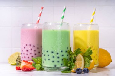 Üç renkli yaz köpüklü çay seti, parlak kremalı inci çayı ya da sütlü tapyoka içecekleri, pembe dut, sarı narenciye, yeşil nane, tapyoka topları ve ezilmiş buz, beyaz arka planda.