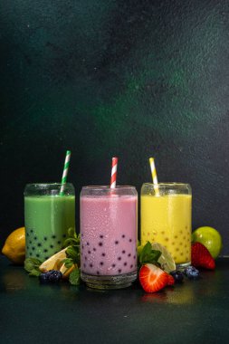 Üç renkli yaz köpüklü çay seti, parlak kremalı inci çayı ya da latte tapyoka içecekleri, pembe dut, sarı narenciye, yeşil nane, tapyoka topları ve ezilmiş buz, koyu arkaplanda.