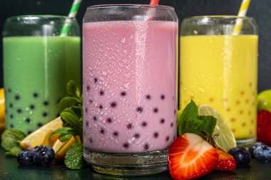 Üç renkli yaz köpüklü çay seti, parlak kremalı inci çayı ya da latte tapyoka içecekleri, pembe dut, sarı narenciye, yeşil nane, tapyoka topları ve ezilmiş buz, koyu arkaplanda.