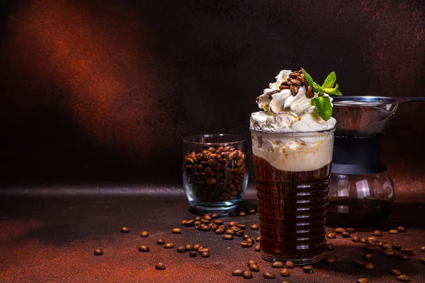 Iced coffee in tall glass. One sweet cold latte with whipped cream, with chemex coffee maker on dark brown background copy space
