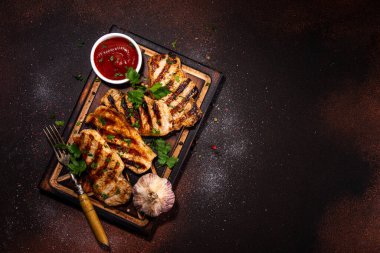  American bbq food concept. Grilled barbeque pork meat steaks with tomato bbq sauce, spices and greens, on cutting board, dark background top view copy space 