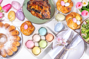 Festivalde Paskalya yemeği veya brunch masası sunuldu, Paskalya yumurtası, lale çiçeği buketi, geleneksel Paskalya yemekleri - pasta, çapraz çörekler, çelenk ekmeği, jöleli jambon ve bahar salatası, beyaz masa arkaplanı