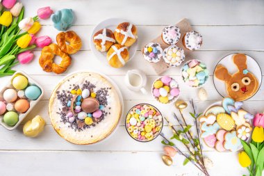 Easter brunch, breakfast food, Kids Easter party buffet. Various traditional Easter sweets, candy, pasties and baking - cross buns, cheesecake, chocolate eggs, pancakes, cupcakes, top view copy space clipart