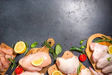 Çeşitli çiğ tavuk eti porsiyonları. Pişmemiş tavuk filetosu, but, kanatlar, şeritler ve bacaklar siyah yemek masasında baharatlı. 