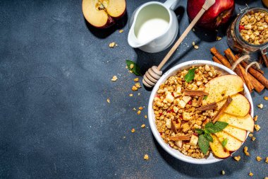 Healthy autumn breakfast granola. Apple pie granola with muesli, cinnamon spices, apples slices, honey and nuts, on black stone background copy space