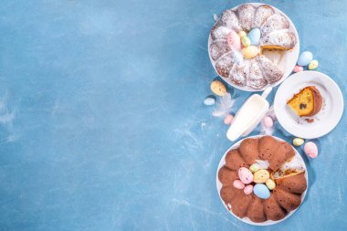 Traditional cake for Easter. Chocolate and vanilla Easter round cake with chocolate and sugar powder sprinkles, colorful Easter eggs, spring flowers, on a blue background copy space
