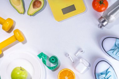 Spring slim and fitness, active living concept. Small yellow dumbbells, bottle of water, sports shoes, scales, salad, fresh vegetables and fruits on a light white background, top view copy space