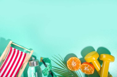 Bahar, yaz zayıflama mevsimi konsepti. Sulu spor şişesi, fitness dambılları, plaj şezlongu dekor, mezura, not defteri, elma, açık mavi arka planda dilimlenmiş turuncu. Düz kopya alanı üst görünümü