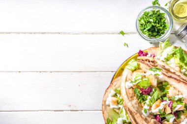 Akdeniz yemekleri. Doner Kebap, Taco, Shawarma, Yunan jiroskop sandviçi, kızarmış tavuk eti, taze sebze, tsatziki sosu. Güneşli beyaz tahta masa kopyalama alanı