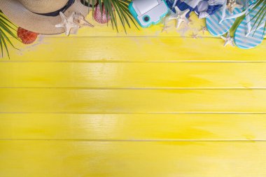 Bright sunny lighted summer vacation background, vacation and travel, beach accessories, swim suit, hat, flip flops, photo camera, sea star and shells on high-colored yellow wooden background top view