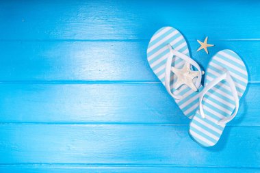 Bright sunny lighted summer vacation background, vacation and travel, beach accessories, swim suit, hat, flip flops, photo camera, sea star and shells on high-colored blue wooden background top view