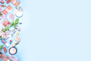Spring make up set on light blue background. Different make-up professional cosmetics, beauty accessories flat lay with spring blossom flowers top view copy space