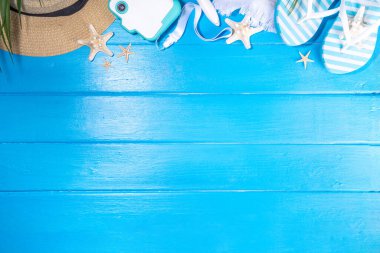 Bright sunny lighted summer vacation background, vacation and travel, beach accessories, swim suit, hat, flip flops, photo camera, sea star and shells on high-colored blue wooden background top view