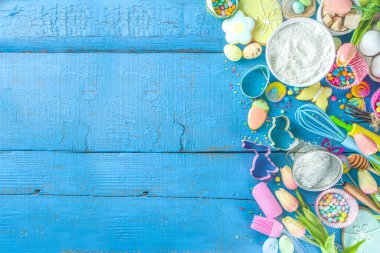 Paskalya pişirme arka planı merdane, çırpma, yumurta, un ve mavi tahta masa manzaralı renkli şeker konfetisi. Metin için kopyalama alanı olan düz uzandı