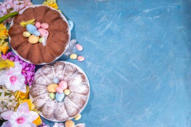 Traditional cake for Easter. Chocolate and vanilla Easter round cake with chocolate and sugar powder sprinkles, colorful Easter eggs, spring flowers, on a blue background copy space