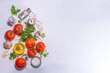 Cooking background with vegetable ingredients. Healthy dinner preparation flat lay, with fresh raw tomatoes, onion, garlic, herbs and greens, olive oil, salt, pepper seasonings, on white background 