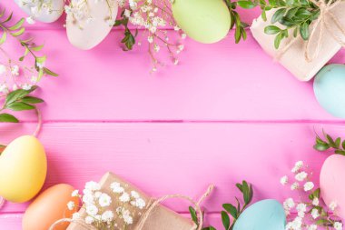 Pembe Paskalya tebrik kartı arka planı bahar çiçekleri, yeşil yaprak dalları ve renkli pastel Paskalya yumurtaları, üst görünüm kopya alanı