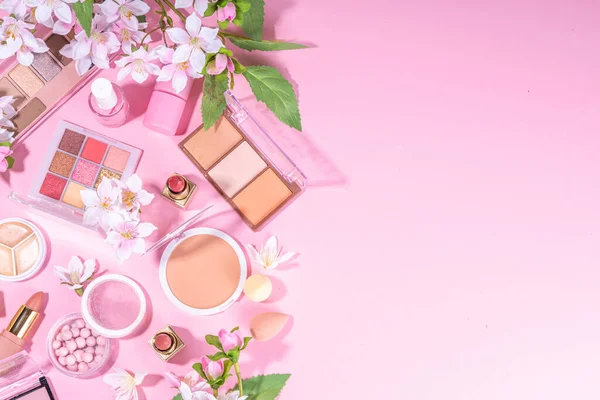 Spring professional makeup flat lay. Spring make up set on pink background. Different make-up cosmetics, beauty accessories flat lay with spring blossom flowers top view copy space