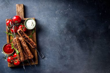Şişe şiş kebap, kıyma etinden. Lula kebap, geleneksel Kafkas tarifi. Siyah beton arka planda, soslar, domatesler ve sebze salatası üst görünüm fotokopi alanı.