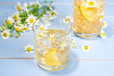 Bitkisel organik soğuk içecek. Çiçek suyu. Buzlu papatya çayı veya limon dilimi ve buz küplü limonata, iki farklı bardakta, mavi ahşap arka plan fotokopi alanı