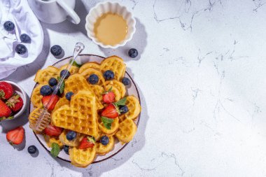 Çilekli, yaban mersinli ve ballı Belçika waffle 'ları, beyaz mutfak masalarında ev yapımı kalp şeklinde waffle' lar.