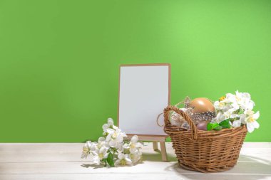 Mutlu Paskalya tebrik kartı arkaplanı, Paskalya yumurtalarının maketi, ilkbahar kiraz çiçekleri küçük sepette, ahşap ve yeşil arkaplan kopyalama alanı