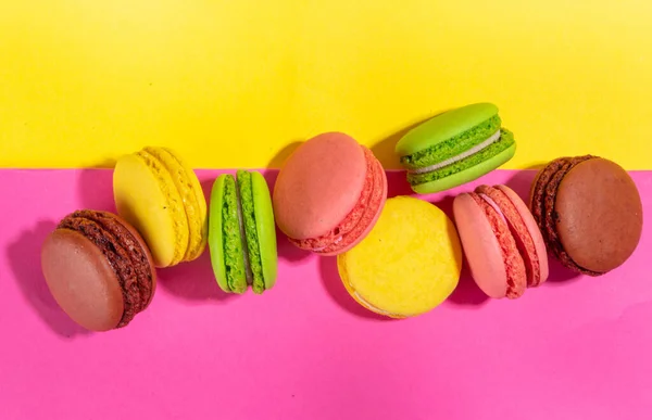 Bright colorful (yellow, pink, green, brown) various flavor macarons sweet cookies on high-colored pink yellow background.  Stack of small french macaron cakes, copy space flatlay
