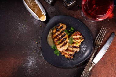 American bbq food concept. Grilled barbeque pork meat steaks with traditional gravy sauce, spices and greens, on plate board, dark background top view copy space 