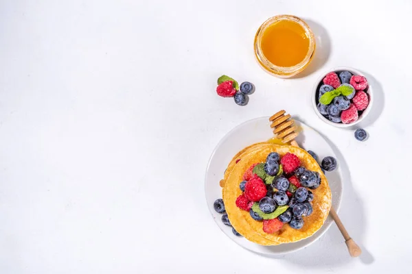 Healthy summer morning breakfast pancakes with fresh berry. Stack of traditional pancakes with blueberry, raspberries, honey. Healthy morning breakfast on white sunny background
