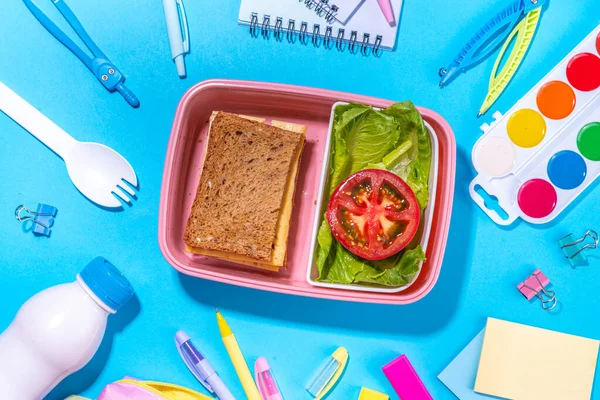 Healthy school meal, back to school concept. Children packed lunch box with balanced diet snack food - yogurt, cereal toast sandwich, apple, fresh vegetable salad, high-colored bright background
