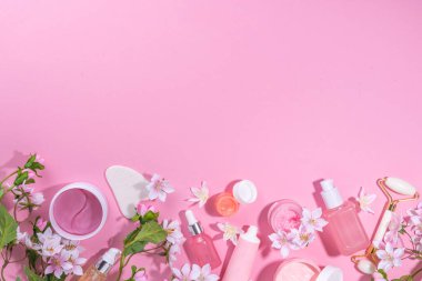 Spring skin care cosmetics flat lay.  Beauty facial care cosmetics: serum, cream, mask on pink sunny background with spring blossom flowers, top view copy space