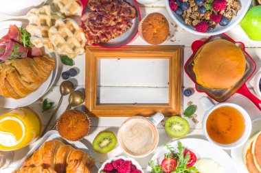 Çeşitli geleneksel kahvaltı yemekleri - domuz pastırmalı kızarmış yumurta, müsli, yulaf, waffle, gözleme, burger, kruvasan, meyve üzümü, kahve, çay ve portakal suyu, beyaz masa arkaplan fotokopisi