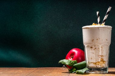 Ev yapımı elmalı turta milkshake, tart parçacıkları ve baharatlı kırmızı sonbahar elma proteini smoothie, sıcacık ahşap arka planda mevsimlik sağlıklı bir kahvaltı içeceği.