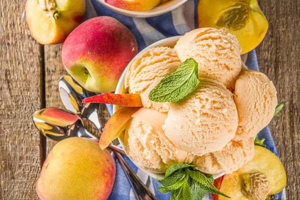 Homemade sweet peach ice cream. Peach gelato balls in small bowls, on wooden background with fresh peaches and mint leaves