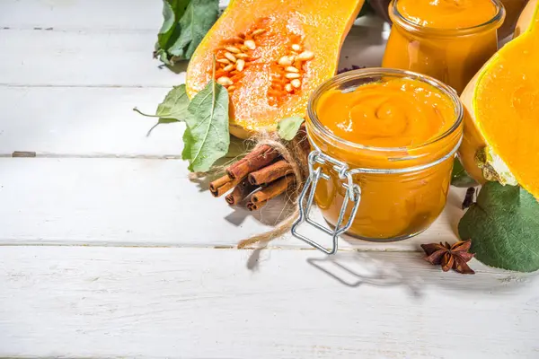 Sweet pumpkin pie jam. Homemade confiture with pumpkin puree and traditional autumn spices. cinnamon, anise. With fresh butternut squash and fall leaves on white wooden background