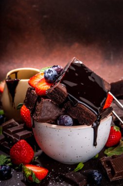 Böğürtlenli siyah çikolatalı kek. Üzerine çikolata sosu serpiştirilmiş ev yapımı kek kurabiyeleri ve koyu arkaplanda taze çilek, yabanmersini, fotokopi alanı.