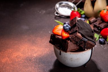 Böğürtlenli siyah çikolatalı kek. Üzerine çikolata sosu serpiştirilmiş ev yapımı kek kurabiyeleri ve koyu arkaplanda taze çilek, yabanmersini, fotokopi alanı.