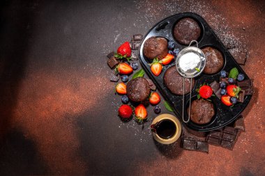 Çilekli çikolatalı kek. Kakao soslu ev yapımı çikolatalı kek tepsisi, şeker tozu ve taze çilek, yabanmersini, koyu kahverengi arka plan fotokopi alanı.